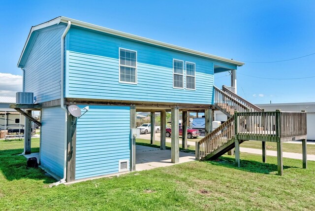 rear view of house with a lawn, central AC, stairway, and a carport