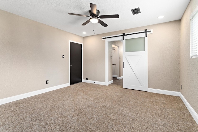 unfurnished bedroom featuring carpet flooring, a barn door, and ceiling fan