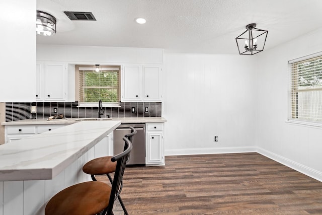 kitchen with dishwasher, sink, decorative light fixtures, white cabinetry, and a breakfast bar area