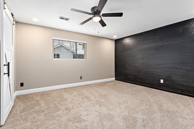 empty room featuring a textured ceiling, a barn door, and light carpet