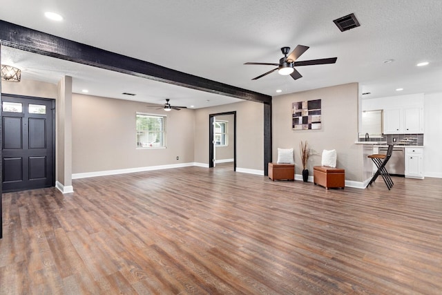 unfurnished living room featuring hardwood / wood-style floors, beam ceiling, and a textured ceiling