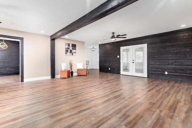 unfurnished living room with beamed ceiling, french doors, hardwood / wood-style floors, and wood walls