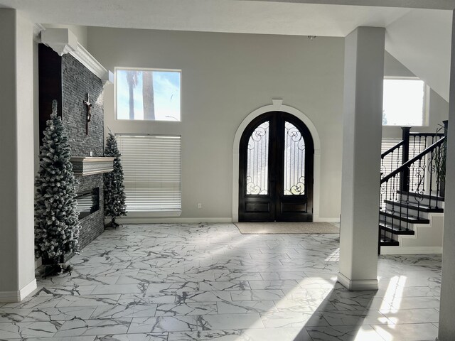 foyer entrance with french doors, a stone fireplace, and a high ceiling