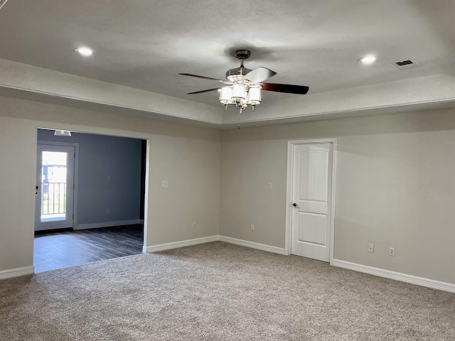 spare room featuring a tray ceiling, ceiling fan, and dark carpet