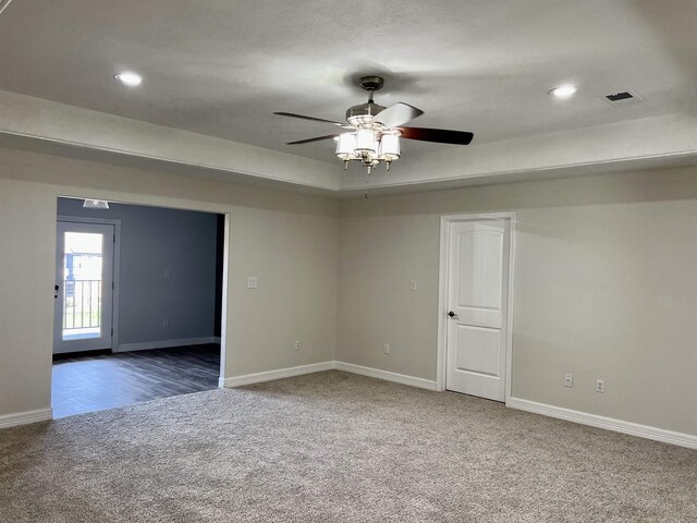 spare room featuring a tray ceiling, ceiling fan, and dark carpet