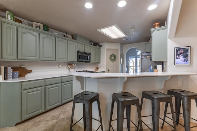 kitchen with a breakfast bar, refrigerator, sink, light tile patterned floors, and kitchen peninsula