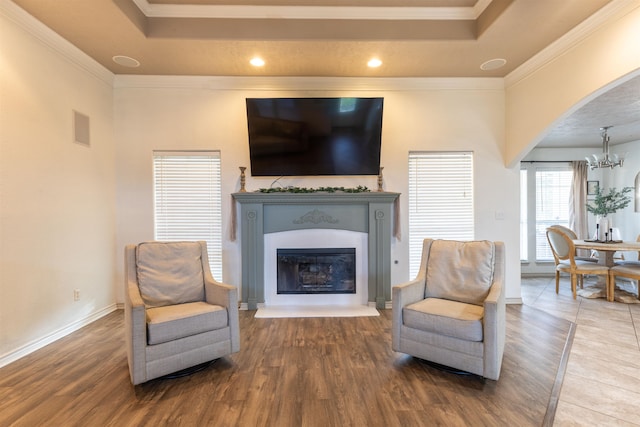 living area featuring a chandelier, wood-type flooring, a tray ceiling, and ornamental molding