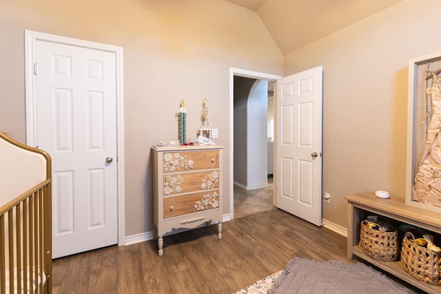 bedroom with a crib, lofted ceiling, and dark hardwood / wood-style floors