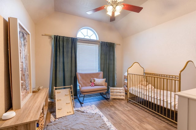 bedroom featuring ceiling fan, wood-type flooring, a crib, and vaulted ceiling