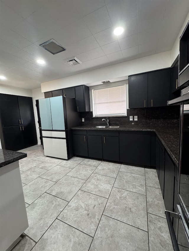 kitchen with light tile patterned floors, sink, backsplash, fridge, and dark stone counters