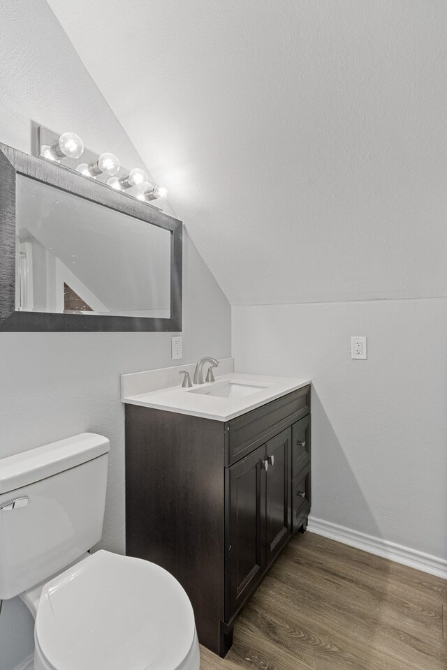 bathroom with vanity, toilet, wood-type flooring, and lofted ceiling