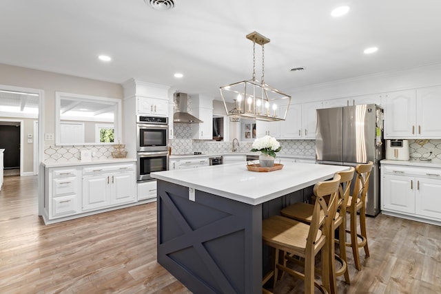 kitchen featuring appliances with stainless steel finishes, wall chimney exhaust hood, decorative light fixtures, white cabinetry, and a kitchen island