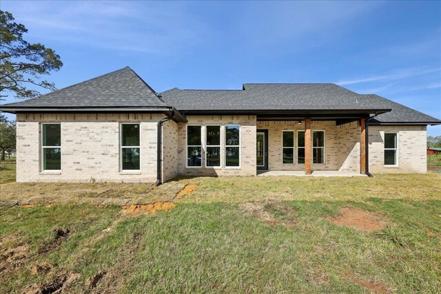 rear view of property featuring a lawn, a shingled roof, and a patio area