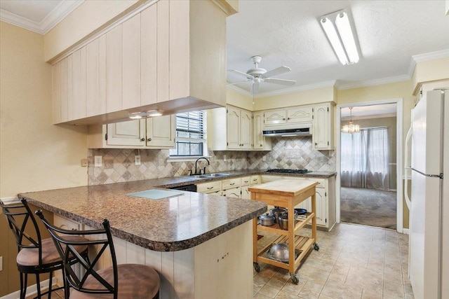 kitchen featuring sink, white fridge, a kitchen bar, kitchen peninsula, and gas cooktop