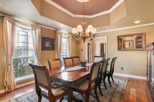 dining space featuring hardwood / wood-style flooring, ornamental molding, a chandelier, and a tray ceiling