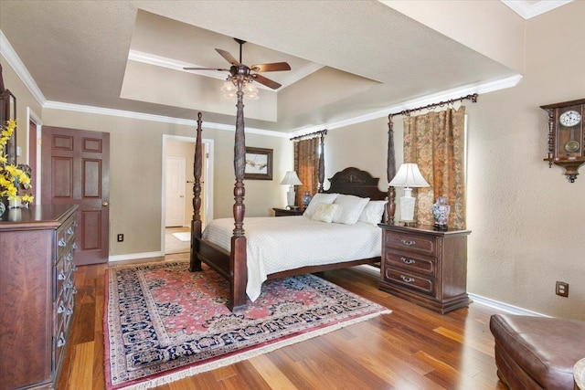 bedroom with ornamental molding, ceiling fan, dark hardwood / wood-style flooring, and a tray ceiling