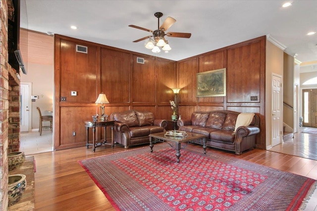 living room with ornamental molding, light hardwood / wood-style floors, ceiling fan, and wood walls