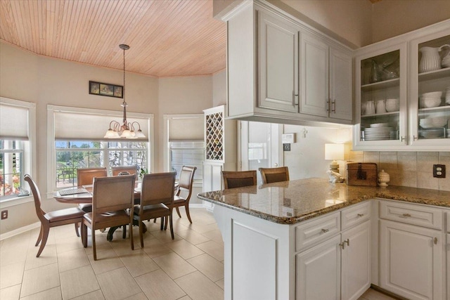 kitchen with white cabinetry, kitchen peninsula, a notable chandelier, pendant lighting, and backsplash