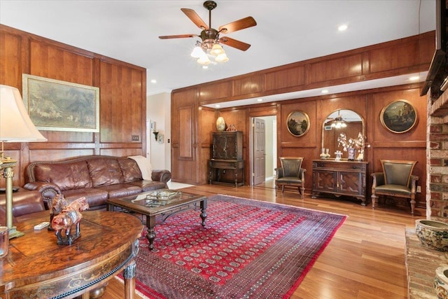 living room with ceiling fan, ornamental molding, light hardwood / wood-style flooring, and wood walls