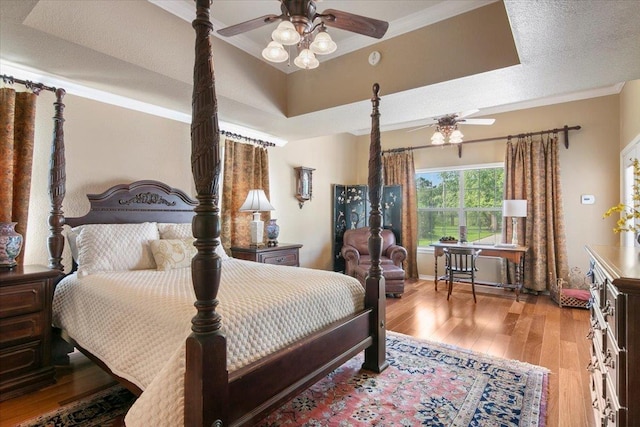 bedroom featuring a tray ceiling, crown molding, light hardwood / wood-style flooring, and a textured ceiling