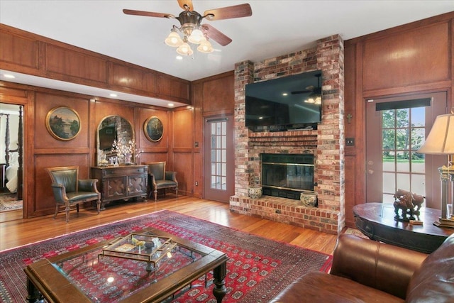 living room featuring wood-type flooring, wooden walls, ceiling fan, and a fireplace