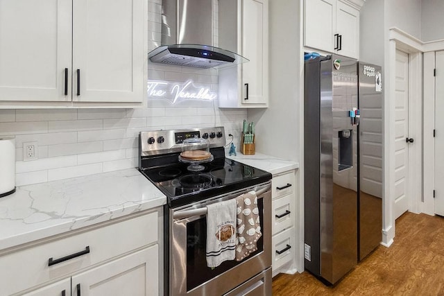 kitchen with white cabinetry, wall chimney range hood, light stone counters, light hardwood / wood-style flooring, and appliances with stainless steel finishes