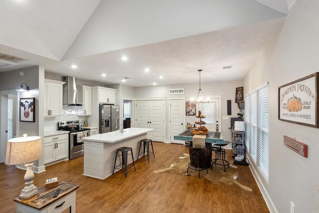 kitchen with white cabinetry, wall chimney exhaust hood, stainless steel appliances, an island with sink, and a breakfast bar