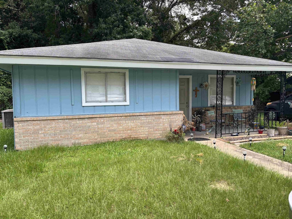 7150 Wall St, Beaumont, TX 77707 - view of front of property featuring a porch, board and batten siding, a front yard, and brick siding