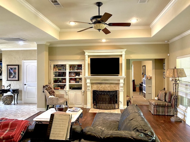 living room with a tray ceiling, a tile fireplace, crown molding, and wood-type flooring