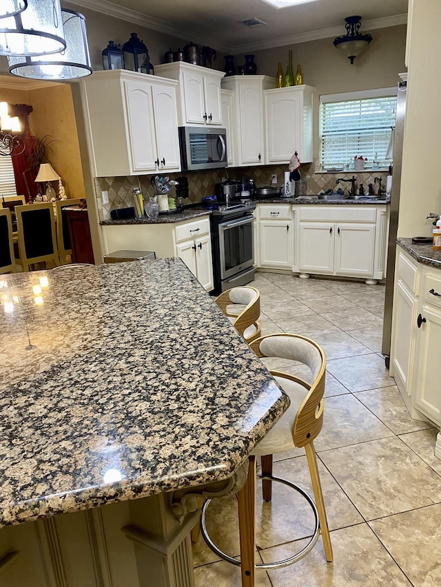 kitchen with dark stone counters, crown molding, decorative backsplash, a kitchen bar, and stainless steel appliances