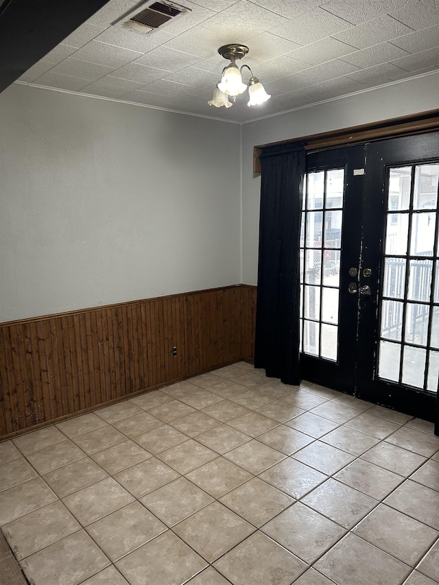 tiled empty room with a chandelier, wooden walls, and french doors