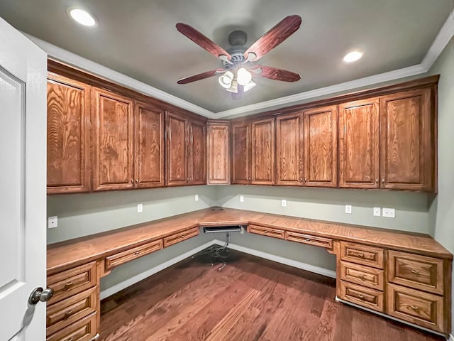 unfurnished office featuring dark hardwood / wood-style flooring, crown molding, built in desk, and ceiling fan