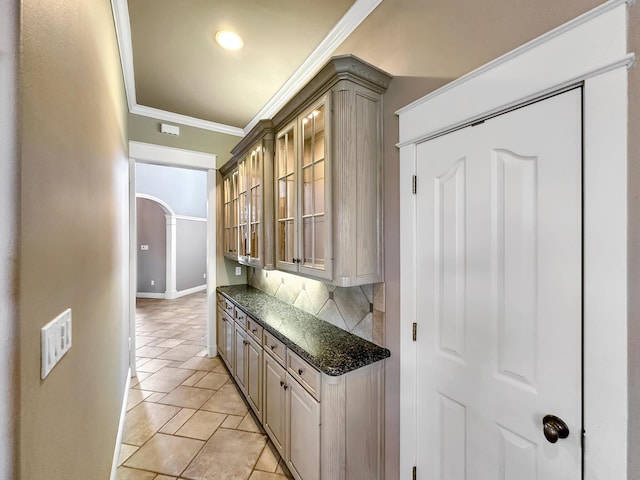 kitchen featuring crown molding, dark stone counters, light tile patterned floors, and backsplash