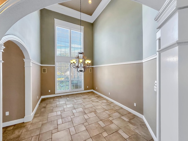 unfurnished dining area with decorative columns, crown molding, a high ceiling, and an inviting chandelier