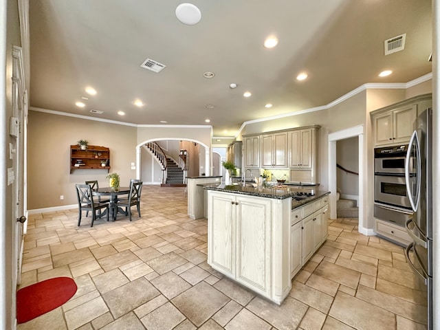 kitchen featuring sink, stainless steel fridge, dark stone counters, cream cabinets, and a center island with sink