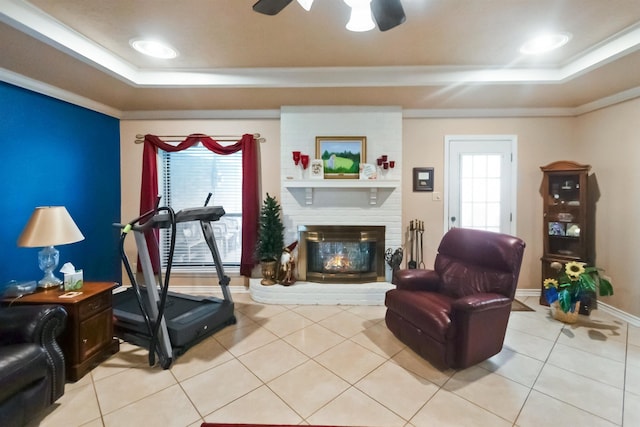 workout room featuring a brick fireplace, a raised ceiling, ceiling fan, crown molding, and light tile patterned flooring