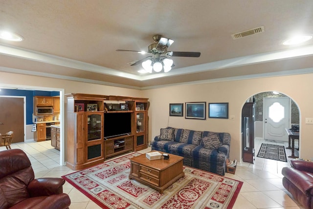 living room featuring light tile patterned floors, a tray ceiling, ceiling fan, and ornamental molding