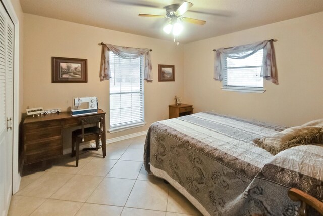 bedroom with multiple windows, ceiling fan, a closet, and light tile patterned floors