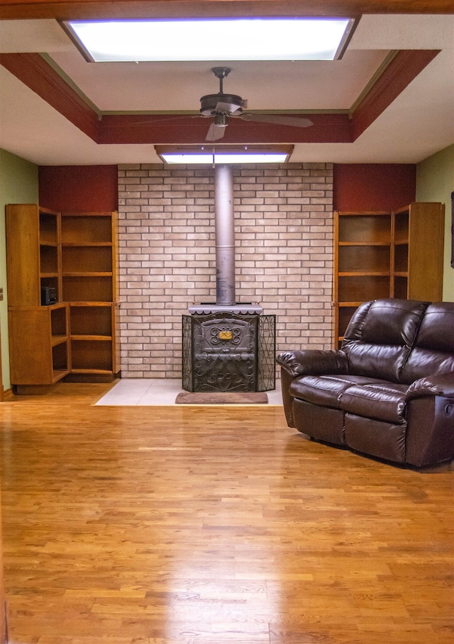 living room featuring a wood stove, light hardwood / wood-style flooring, a raised ceiling, and crown molding