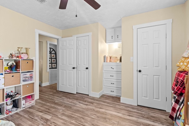 recreation room with baseboards, a ceiling fan, a textured ceiling, and light wood-style flooring