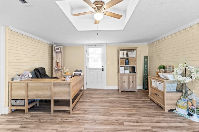 home office featuring brick wall, light wood-type flooring, a ceiling fan, visible vents, and a skylight