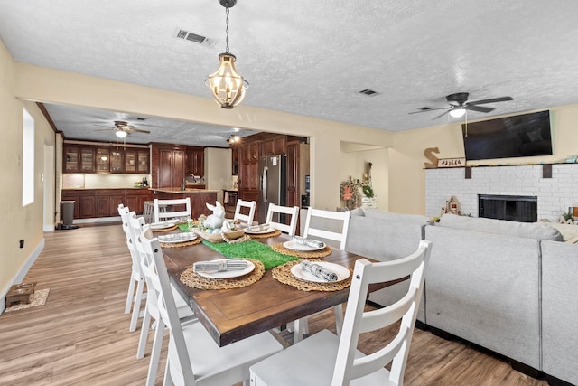 dining area featuring a textured ceiling, visible vents, light wood-style floors, and ceiling fan with notable chandelier