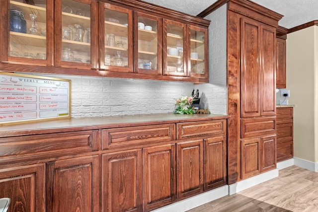 bar featuring tasteful backsplash, ornamental molding, a textured ceiling, and light wood-style flooring