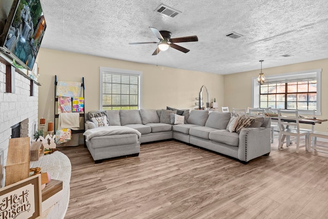 living room featuring visible vents, a ceiling fan, light wood-style floors, and plenty of natural light