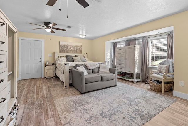 bedroom with a textured ceiling, ceiling fan, light wood-style flooring, and baseboards