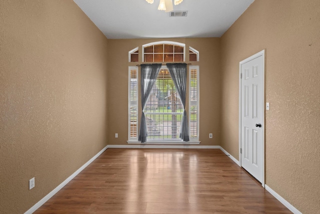 unfurnished room featuring a textured wall, wood finished floors, and baseboards