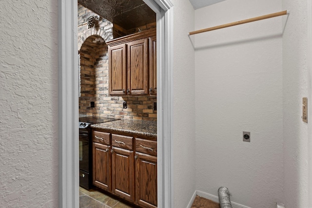 washroom with electric dryer hookup, a textured wall, and cabinet space