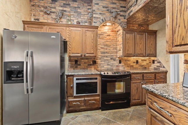 kitchen featuring stainless steel appliances, brown cabinetry, stone tile floors, and light stone counters