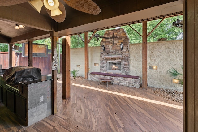 deck featuring an outdoor stone fireplace, fence, area for grilling, and a ceiling fan