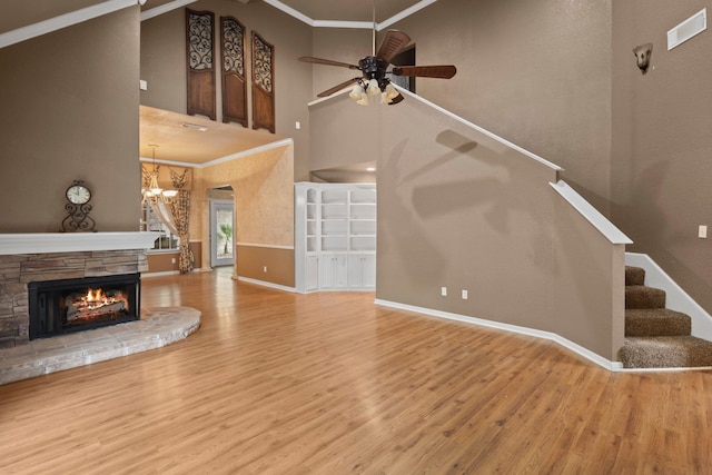 unfurnished living room featuring a high ceiling, wood finished floors, a chandelier, a ceiling fan, and crown molding